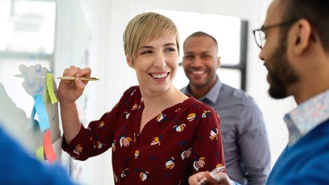 Bild zum Thema Junge Lehrerin mit zwei anderen Lehrern vor einem Whiteboard im Gespräch