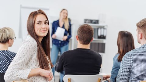 Bild zum Thema Eine Workshop-Gruppe, in der sich eine Teilnehmerin gerade dem Betrachter zuwendet