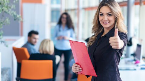 Eine junge Frau mit einer roten Mappe in der Hand, die den Daumen hochstreckt