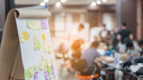 Bild zum Thema Flipchart mit Post-Its; im Hintergrund eine Arbeitsgruppe