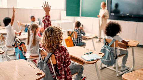 Bild zum Thema Klassenraum mit Schülern; im Hintergrund eine Lehrerin vor der Tafel