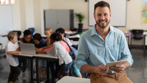 Junger Lehrer im Klassenzimmer; im Hintergrund arbeiten Schülergruppen