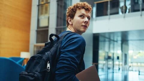 Bild zum Thema Student, der beim Gehen durch ein Unigebäude nach hinten schaut
