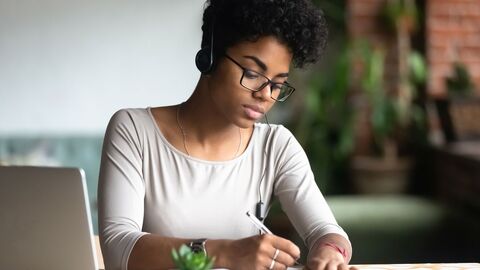 Eine Frau, die gerade einen Text übersetzt; sie sitzt am Schreibtisch und schreibt