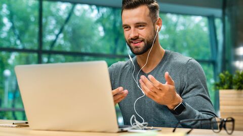 Bild zum Thema Dolmetscher zuhause vor seinem Notebook bei der Arbeit; er hat einen Kopfhörer auf und gestikuliert beim Sprechen