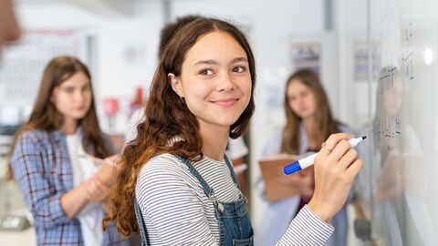 Schülerin, die mit einem Stift etwas an einem Whiteboard berechnet 
