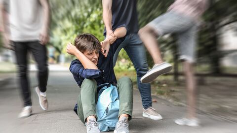 Bild zum Thema Ein Junge sitzt mit erhobenen Händen am Boden und wird von zwei weiteren Kindern geschlagen und getreten.