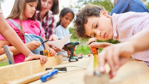 Bild zum Thema Kinder mit ihrer Lehrerin beim Werken mit Holz und Handwerkszeug
