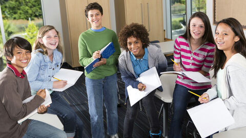 Eine Gruppe von Schülern beim gemeinsamen Lernen; alle haben aufgeschlagene Hefte in der Hand