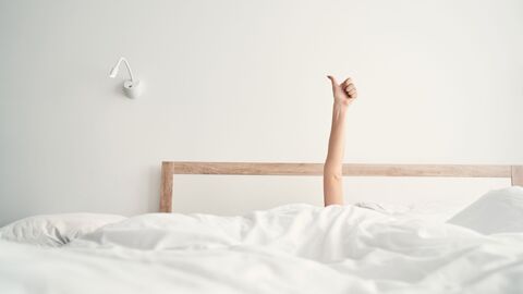 Ein Bett, aus dem ein Arm mit einem ausgestreckten Daumen hochragt