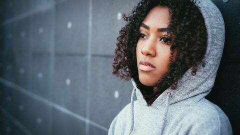 Nachdenkliche, traurige Schülerin, die sich mit dem Rücken an einer Wand anlehnt und in die Ferne blickt 