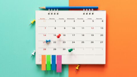 Kalender mit Stift und Pinnadeln auf buntem Hintergrund