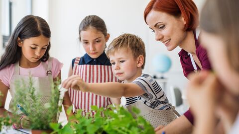 Bild zum Thema Eine Gruppe jüngerer Schüler, die mit einer Lehrerin gemeinsam kochen