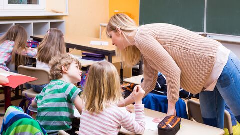 Bild zum Thema Eine Lehrerin hilft gerade einer Bank mit zwei Schülern während des Unterrichts