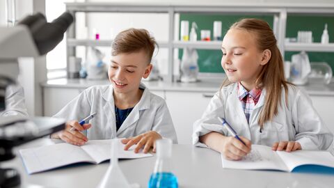 Zwei Schüler im naturwissenschaftlichen Unterricht, die gerade Notizen zu Experimenten in ein Heft schreiben 