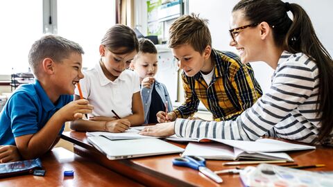 Schüler sitzen mit einer Lehrerin gemeinsam an einem Tisch und schauen sich Lernmaterial an