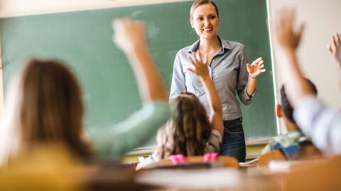 Befragungsportal Lehrerin vor einer Klasse im Unterricht; die Schüler melden sich