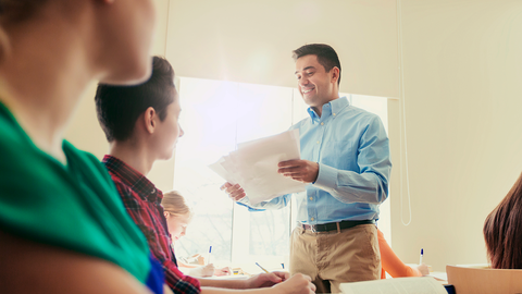 Ein Lehrer teilt gerade Arbeitsblätter im Unterricht aus