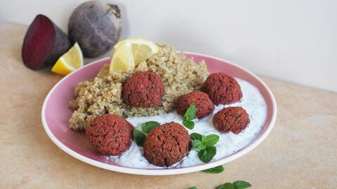 Rote Beete Falafel mit Zitronenquinoa und Minz-Dip auf einem Teller. Einige der Zutaten im Hintergund angeordnet.