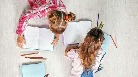 Sprachbildung und Leseförderung Zwei Kinder liegen auf dem Boden: eines liest, eines schreibt