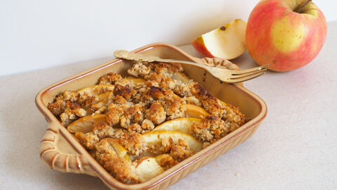 Apple-Crumble mit Nuss-Streuseln und einem Apfel im Hintergrund