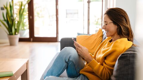 Eine Lehrerin zuhause auf dem Sofa schaut in ihr Handy
