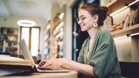 Eine Studentin tippt am Notebook in der Bibliothek