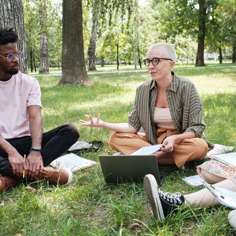Bild zum Thema Eine Gruppe Lehrkräfte, die draußen in einem Park auf einer Wiese sitzt und gerade etwas zusammen erarbeitet