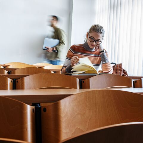 Bild zum Thema Eine jugendliche Schülerin in einem sich leerenden Klassenzimmer, die gerade in ihren Unterlagen blättert